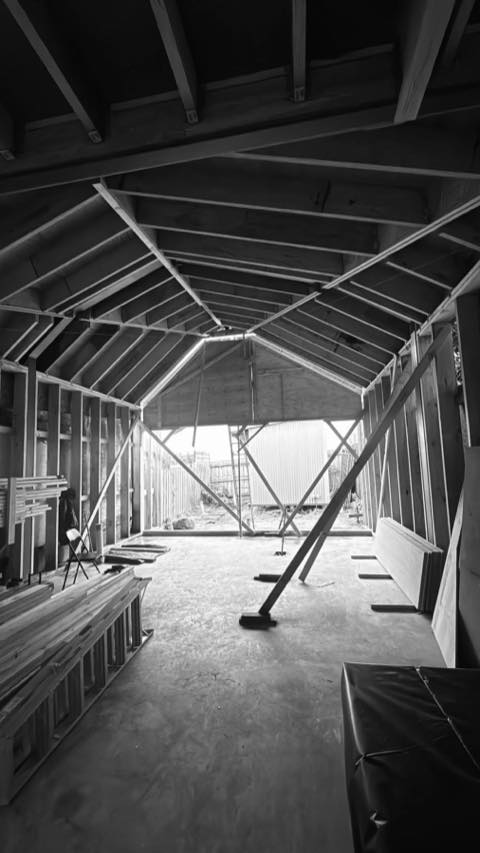 Black-and-white view of timber wall and roof framing inside a new build