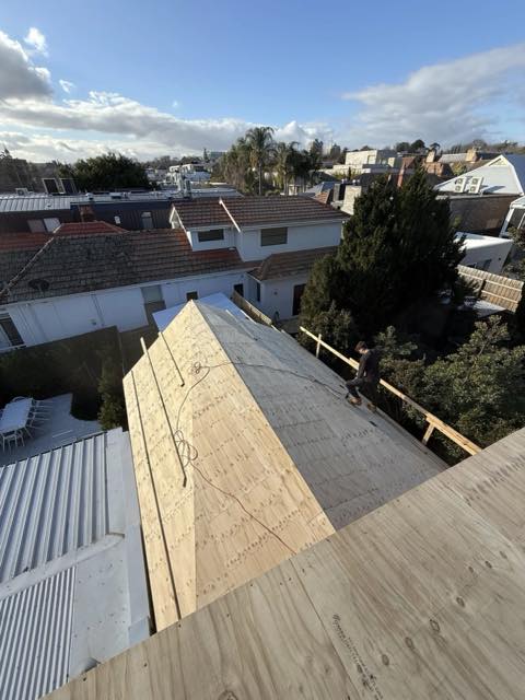 Carpenter fixing plywood sheathing to a new roof structure